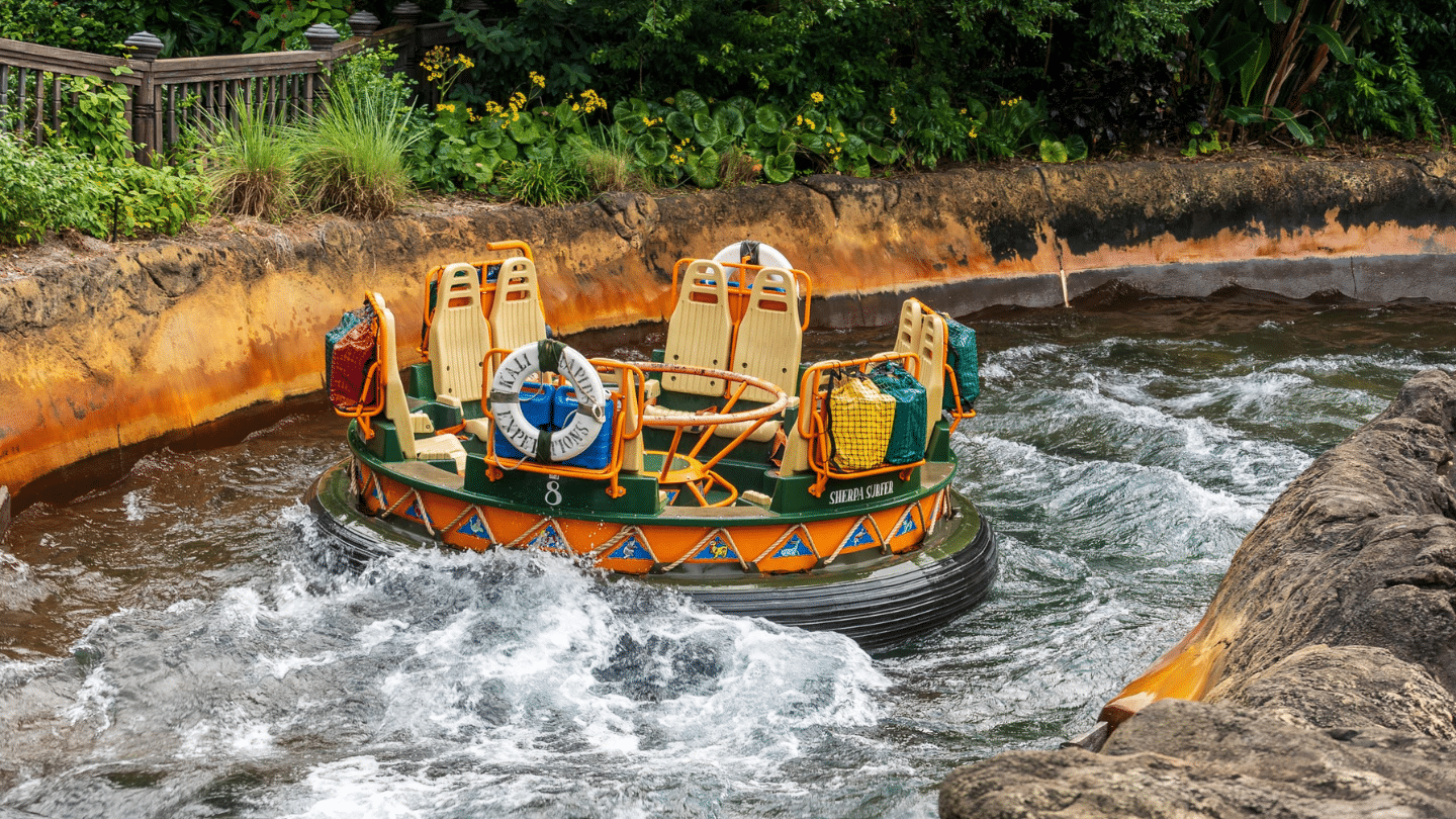 empty circular river raft ride moves through churning water between rocky banks and lush green plants in a theme park channel