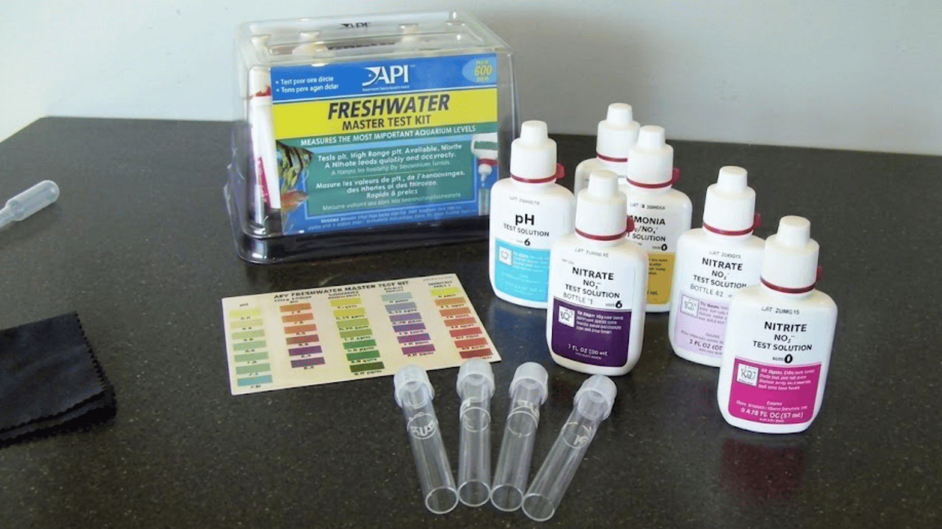 freshwater aquarium test kit with reagent bottles test tubes and color chart arranged on a dark countertop surface