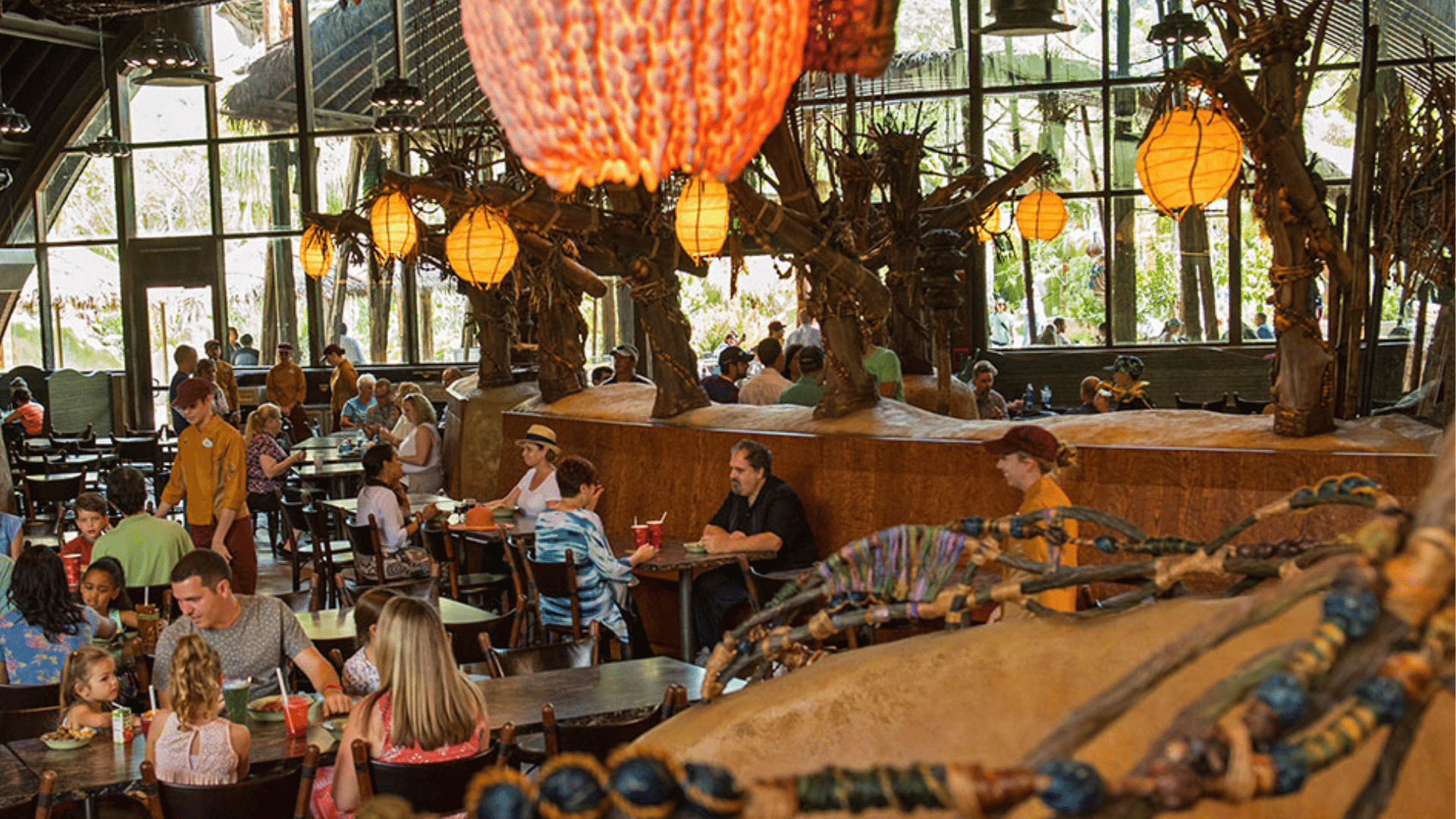 guests dine inside a themed animal kingdom restaurant with glowing lanterns rustic decor and large windows surrounding seating areas