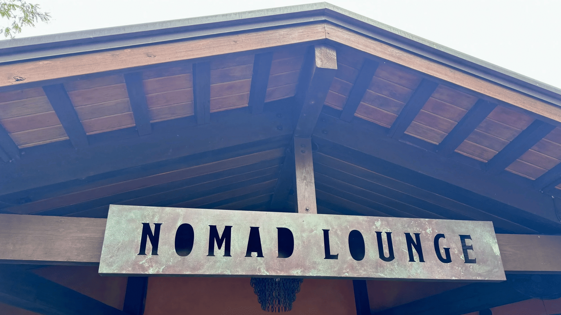 nomad lounge entrance with a large metal sign beneath a wooden roof at a themed outdoor dining location