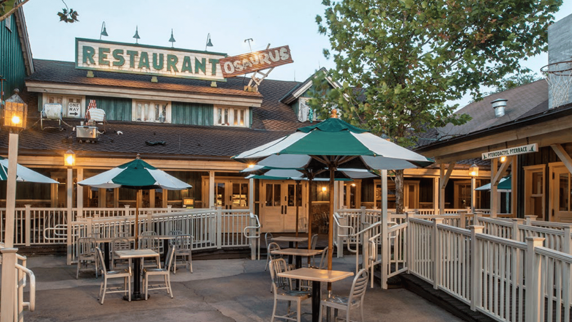 outdoor seating area at restaurantosaurus with shaded tables white railings and a large restaurant sign at dusk
