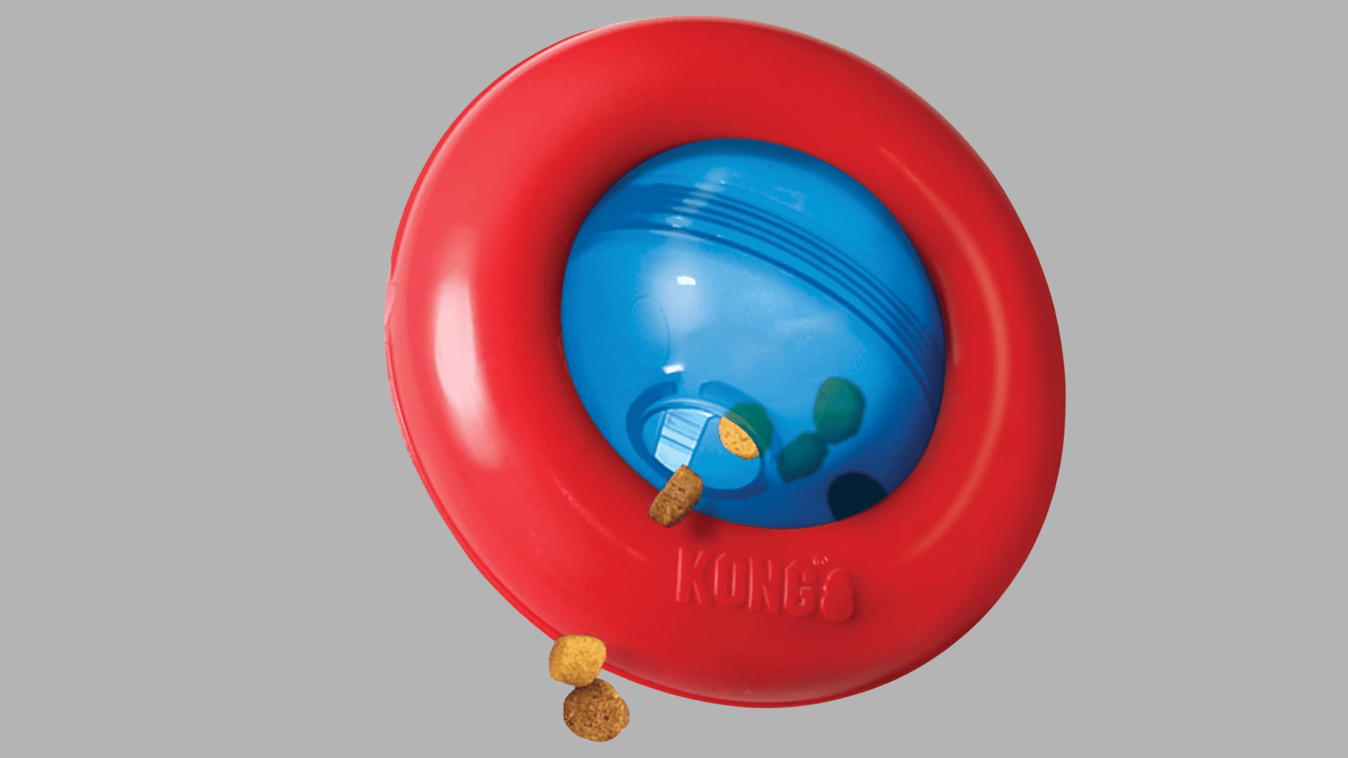 red ring shaped dog toy with blue treat dispensing ball in the center and kibble pieces visible near the opening