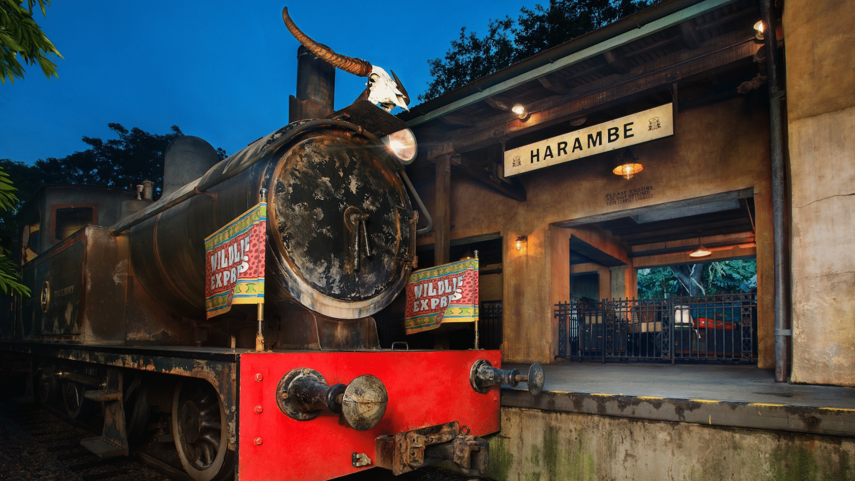 rustic steam locomotive parked beside the harambe station entrance with wildlife express banners glowing at dusk