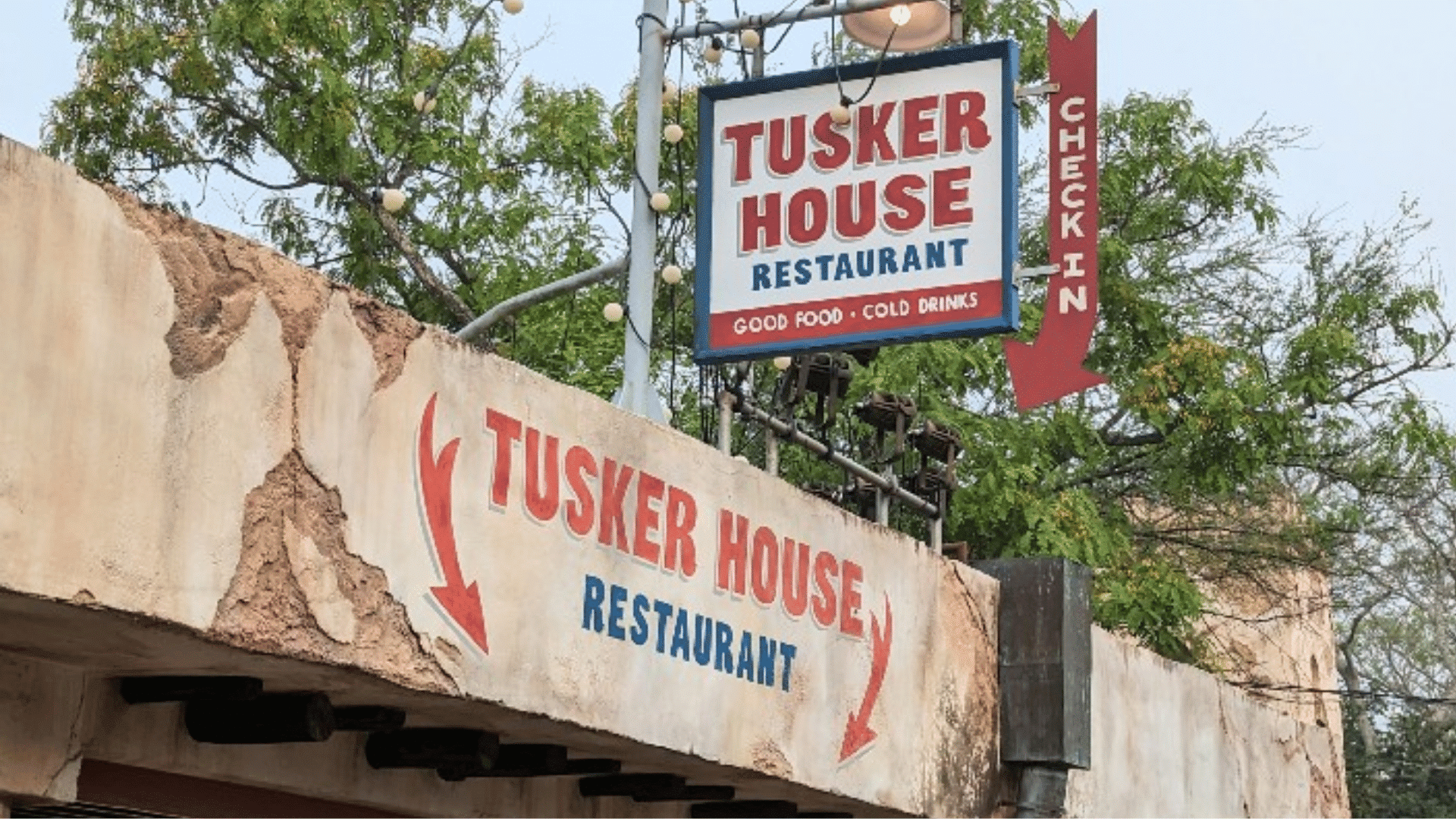 tusker house restaurant entrance with hanging sign and outdoor seating area surrounded by trees in a theme park setting
