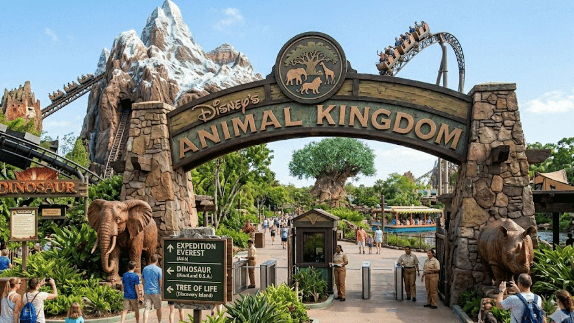 visitors walk beneath disney animal kingdom entrance with mountain coaster and safari themed sculptures nearby