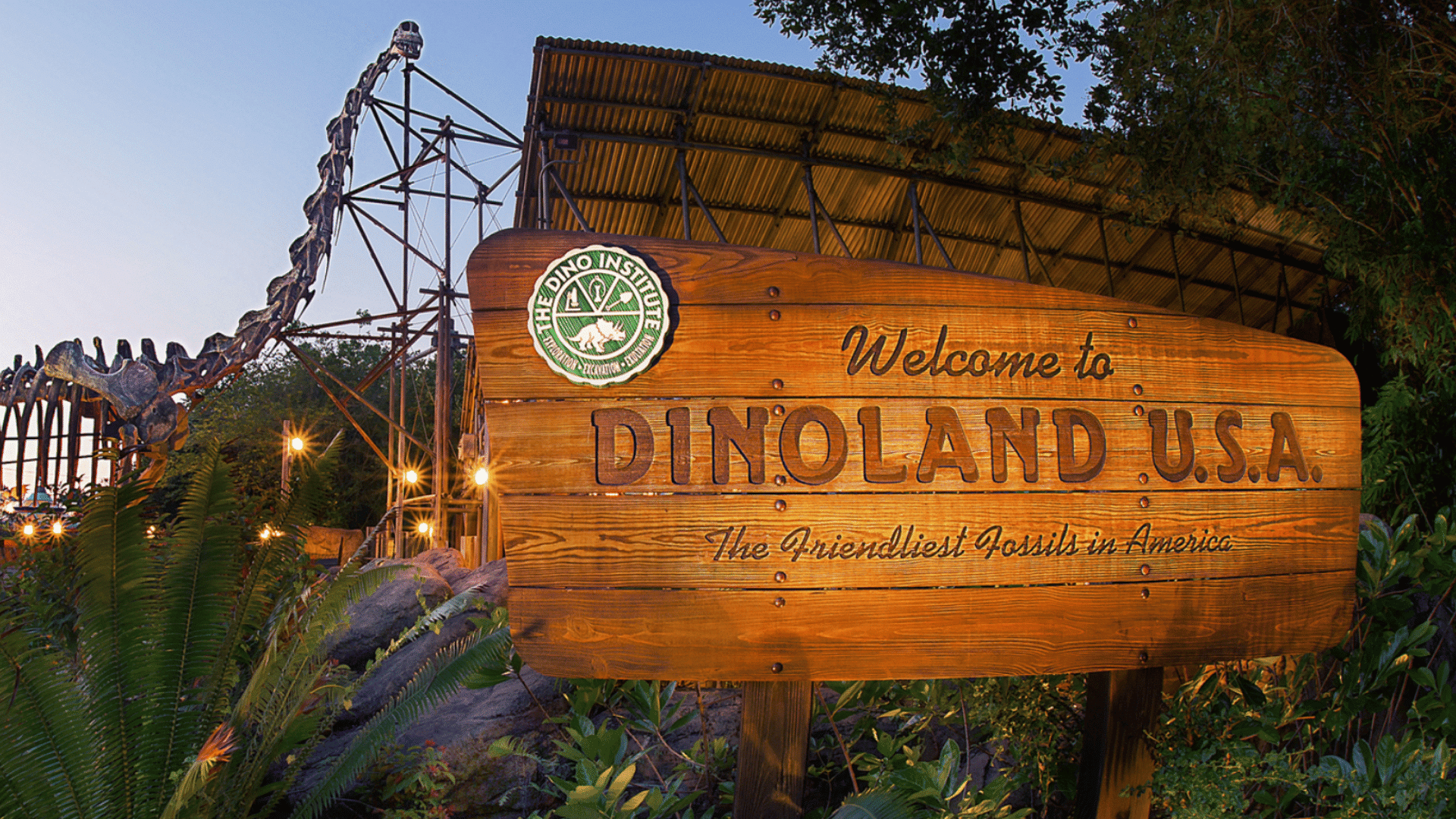 wooden dinoland usa welcome sign stands beside dinosaur skeleton display surrounded by tropical plants at animal kingdom