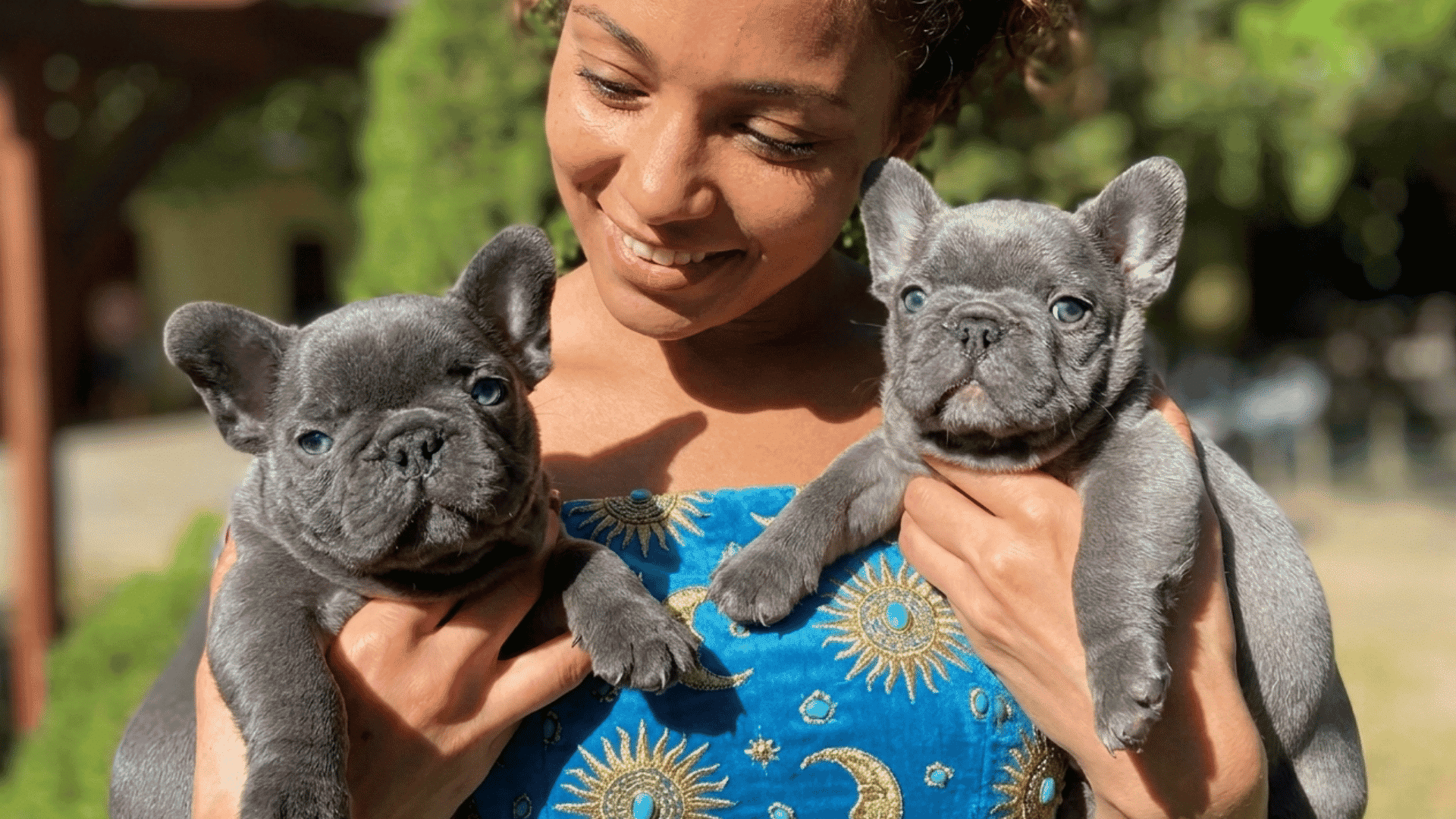 a smiling woman holds two rare French bulldog puppies in a sunny garden