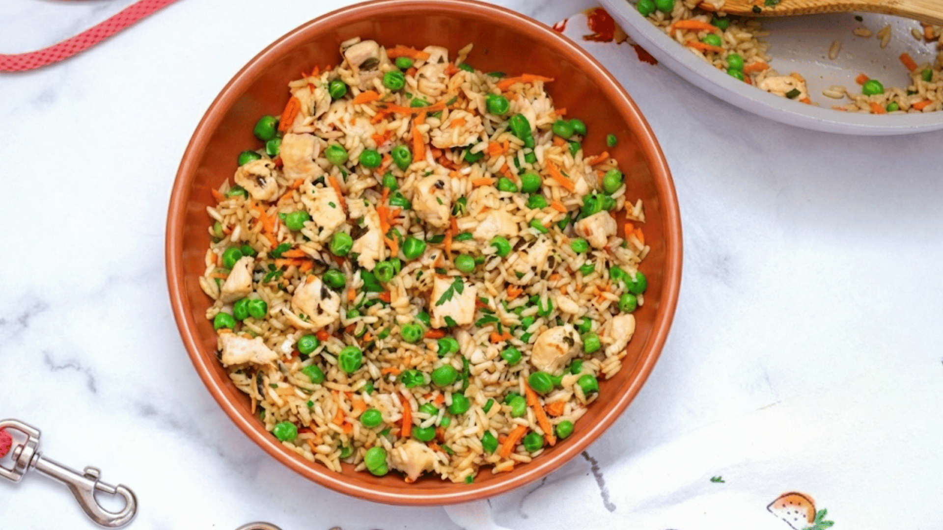 bowl of chicken fried rice with peas carrots and mushrooms served on a marble countertop beside a skillet with more rice