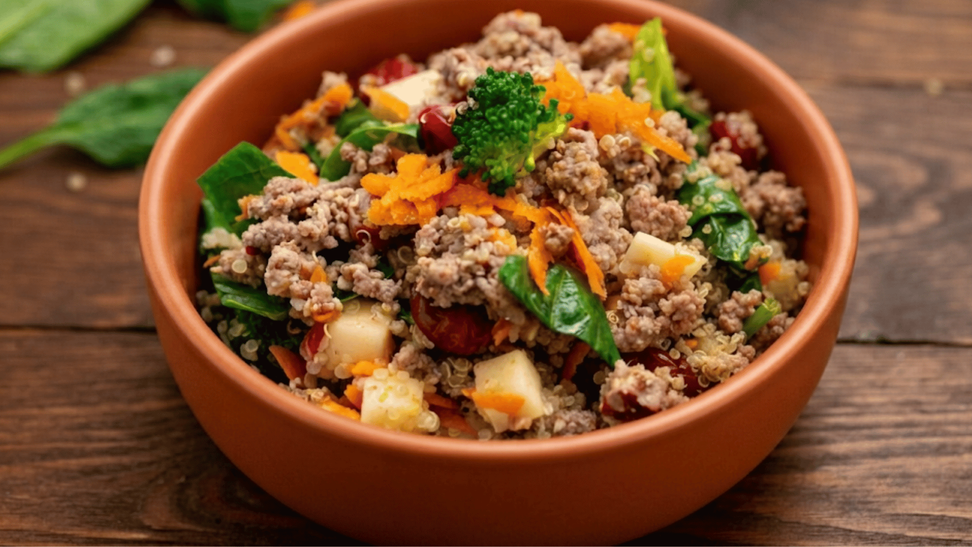 bowl of ground beef quinoa spinach broccoli carrots apples and cranberries served as a colorful healthy meal on a wooden table