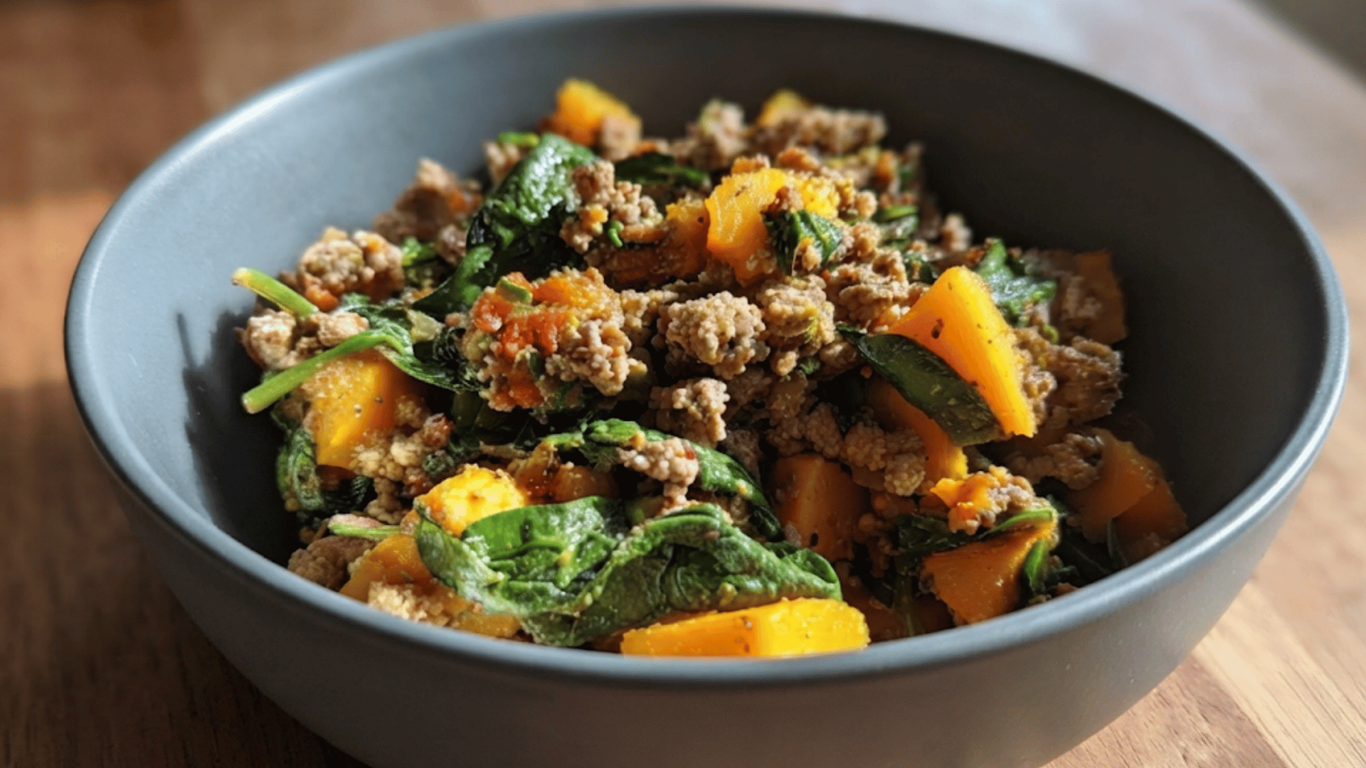 bowl of ground beef with spinach roasted squash and quinoa served as a hearty nutritious homemade meal on a wooden table