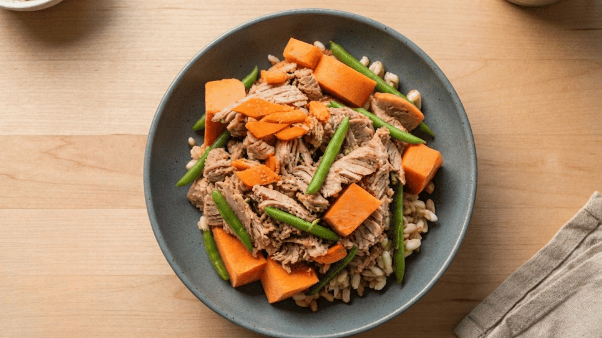 bowl of shredded beef with sweet potatoes green beans and brown rice served on a wooden table as a hearty balanced meal