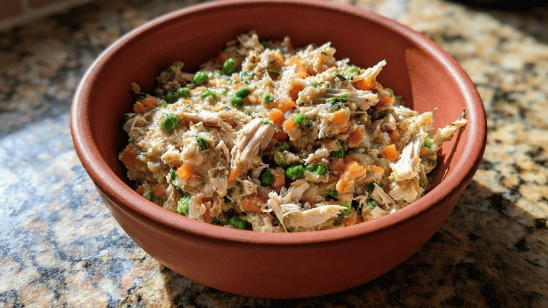 bowl of shredded chicken with peas carrots broccoli and quinoa served as a creamy nutritious homemade meal on a granite countertop