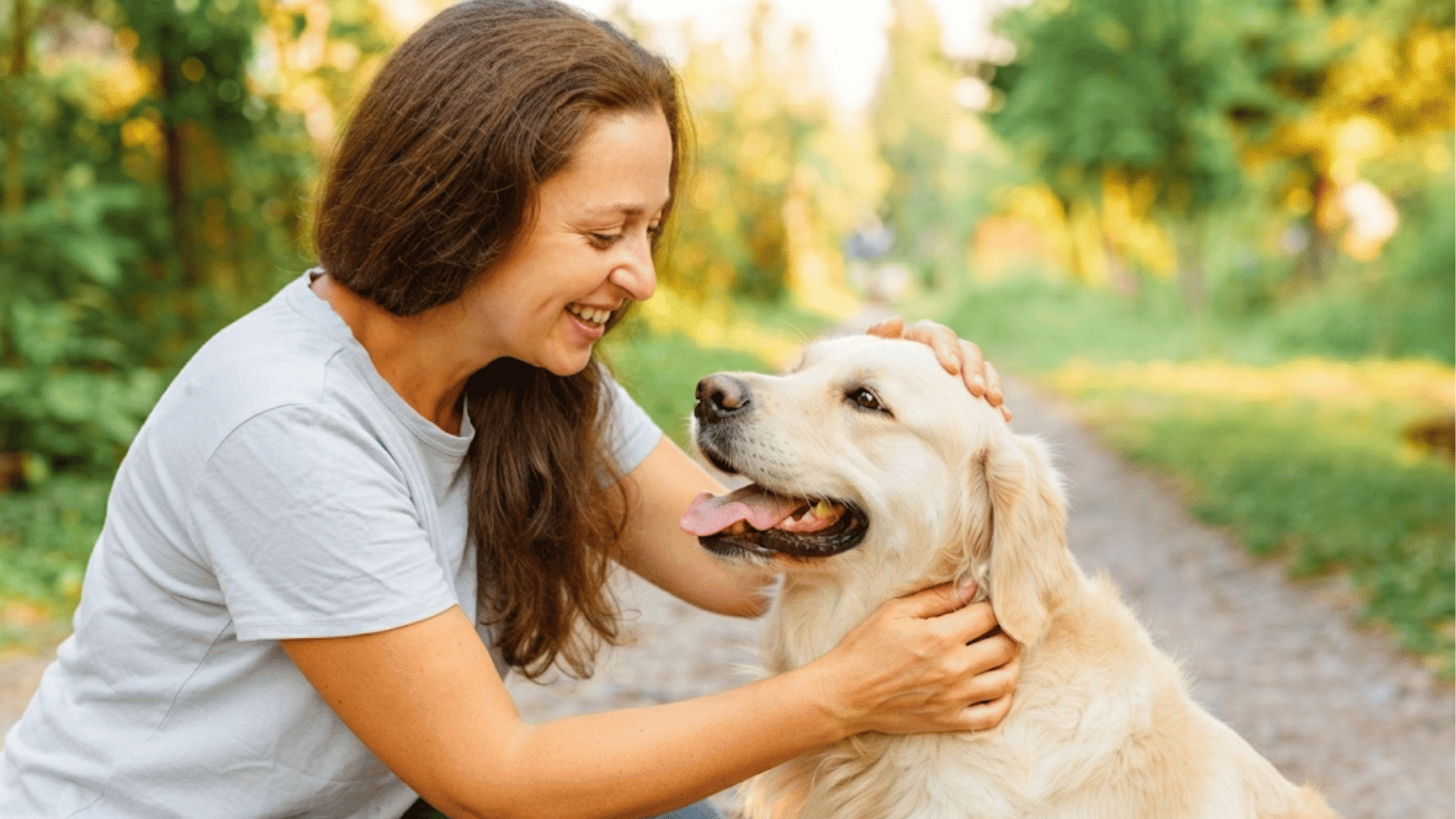 person smiling while gently petting a happy dog outdoors on a green trail during a peaceful moment